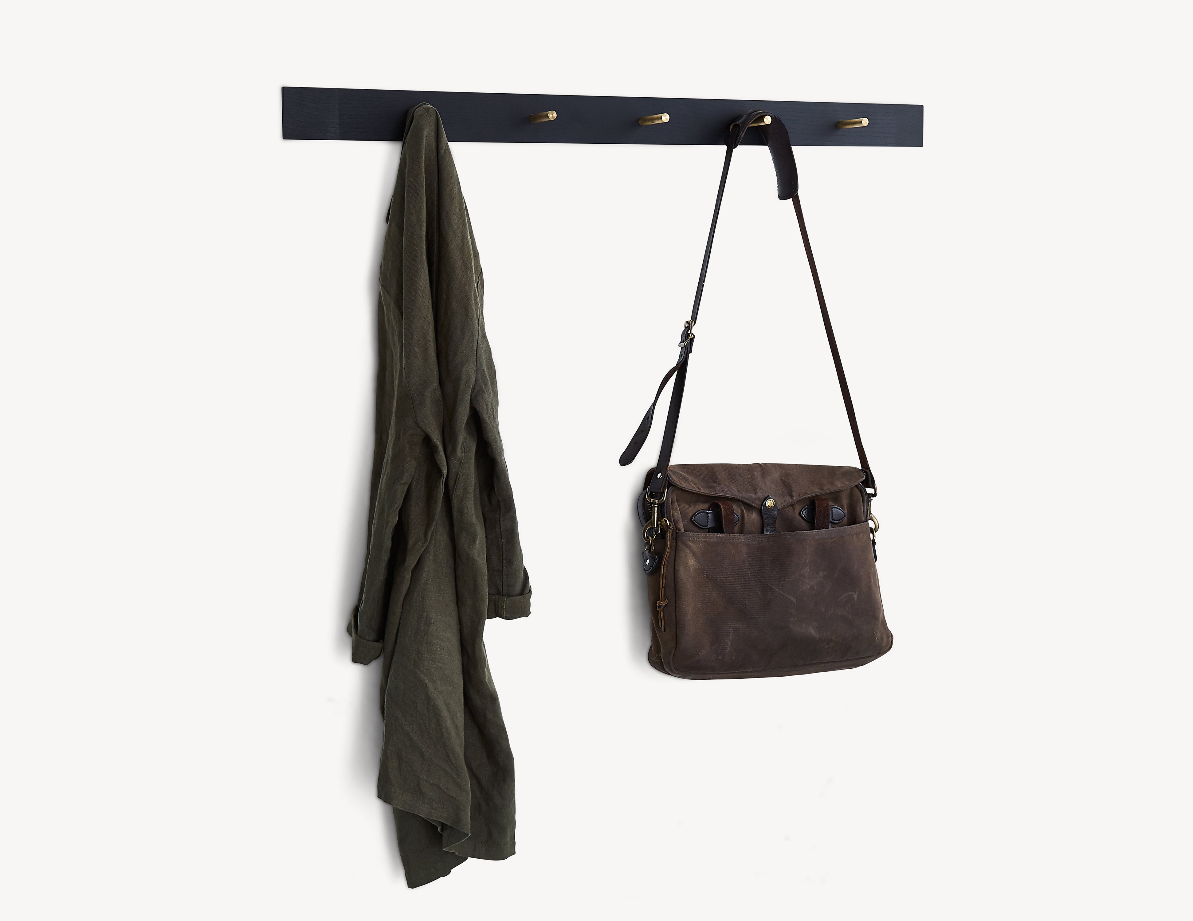 black wooden rail with brass pegs. a bag and a coat hanging on two of the pegs.