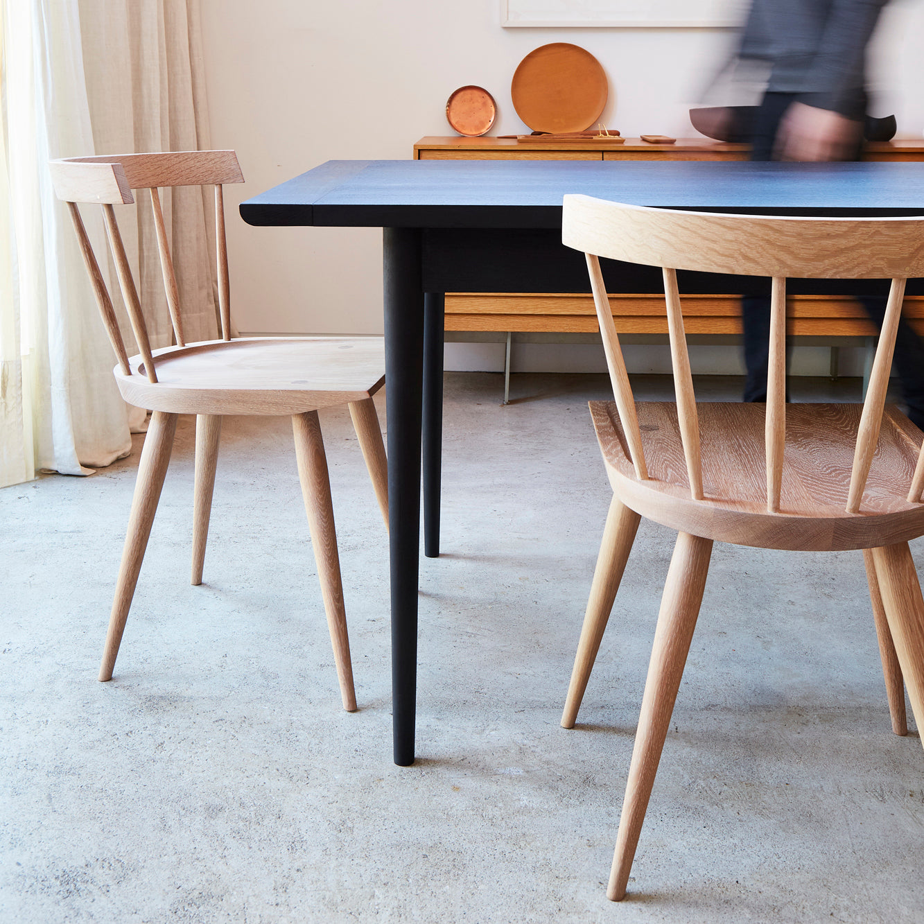 minimal dining room scene with a black wooden table and two light wood chairs. 