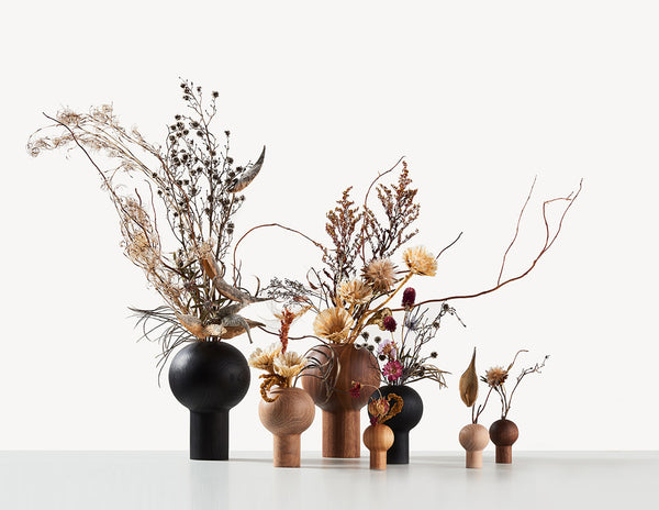 An assortment of round wooden vases in different sizes and colours, with Ikebana flower arrangements.