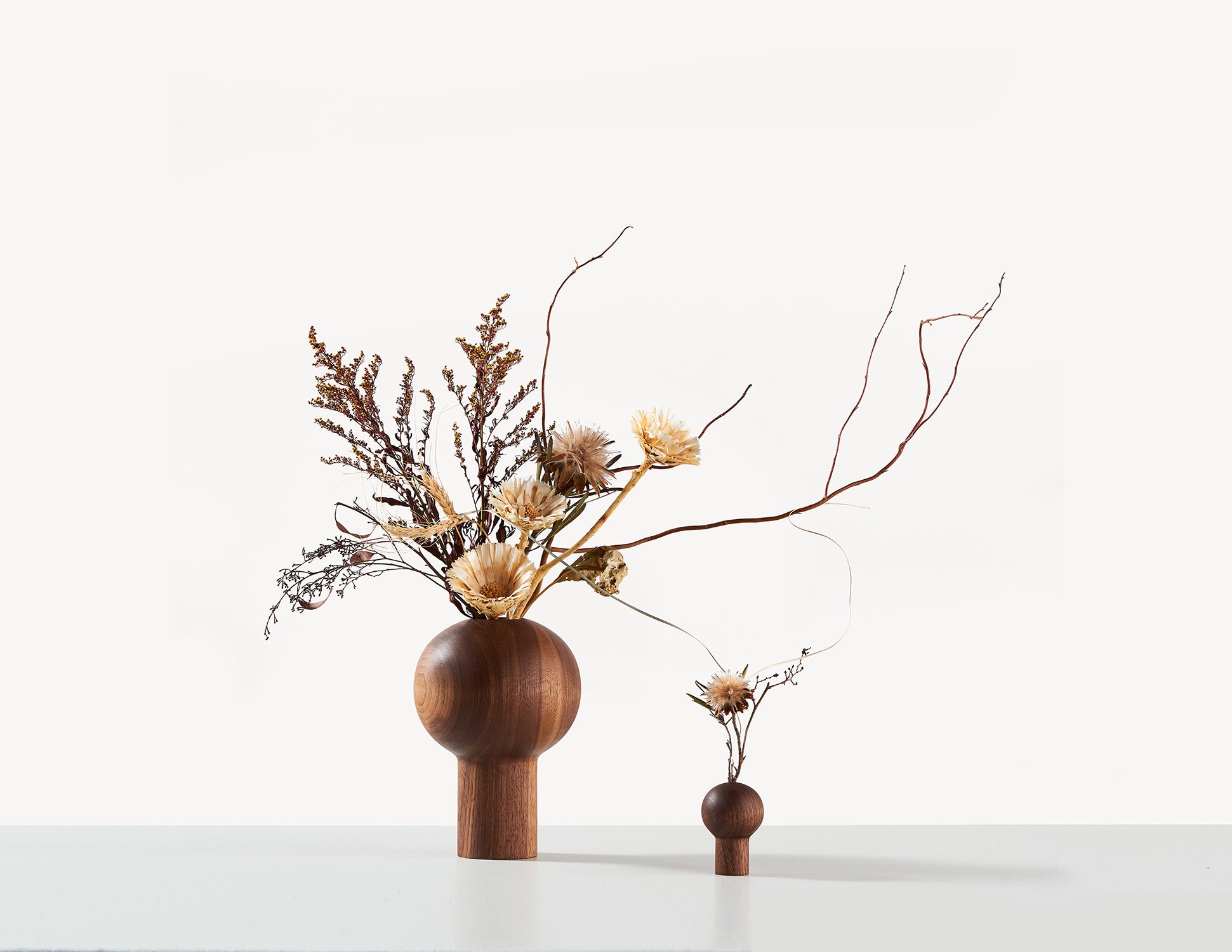 two round wooden dry vases in walnut wood, with Ikebana flower arrangements.