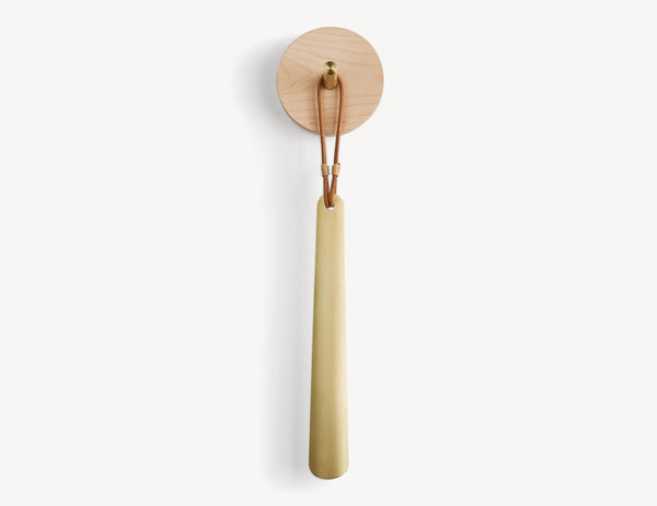 round light wood disc with brass peg.  a brass shoe horn hanging from the peg with a leather loop.